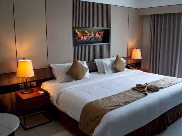 A well-lit hotel room with a neatly made bed, bedside lamps, and a small table by the window. Neutral, modern décor with ambient lighting.
