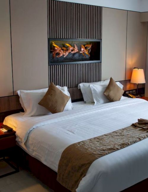A cozy hotel room with a neatly made double bed, two bedside lamps, a wall decoration, and a window with closed curtains.