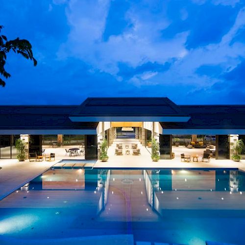 An elegant outdoor pool area of a luxury resort at dusk with modern architecture and ambient lighting, surrounded by lounge chairs.