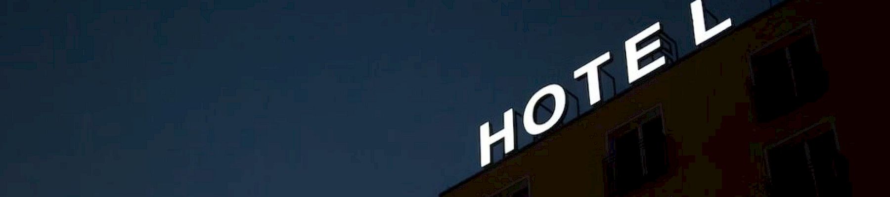 The image shows the side of a building at night with a lit sign spelling "HOTEL" in bright white letters on its roof's edge.
