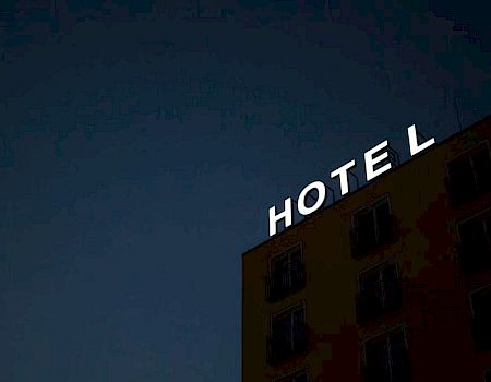 The image shows the side of a building at night with a lit sign spelling "HOTEL" in bright white letters on its roof's edge.