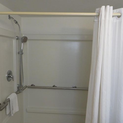 This image shows a white shower area with a curtain, a showerhead, grab bars, and a towel hanging on one of the grab bars.