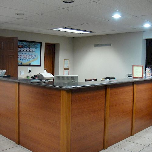 The image shows a reception desk in an office or hotel lobby area, equipped with phones and office supplies, with a poster on the wall.