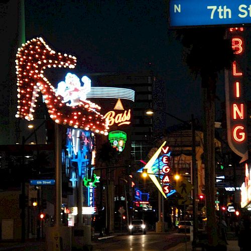 The image shows a street at night with neon signs, including a high heel shoe, "Vegas" arrow, "Bling," and a street sign for N 7th Street.