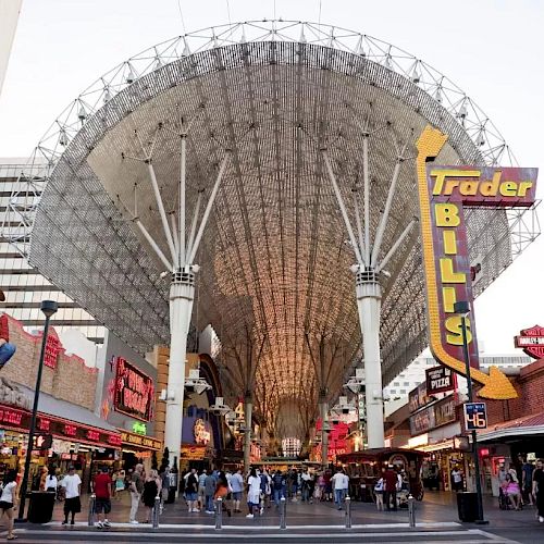 The image shows a bustling street under a large, lit canopy with signs and shops, including one for Trader Bill's. People are walking and exploring.