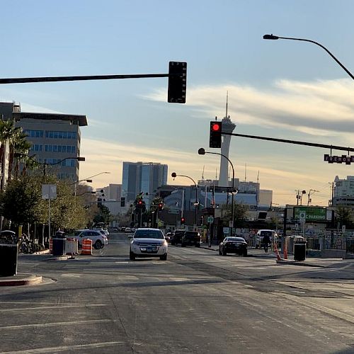 Urban street view with cars stopped at a red light, buildings in the background, and the Stratosphere Tower visible in the distance.