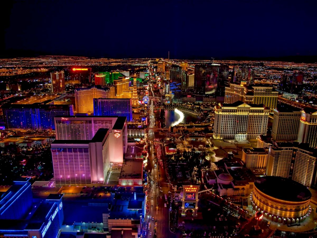 An aerial view of a brightly lit city with numerous buildings and neon lights, likely depicting a famous strip in Las Vegas at night.