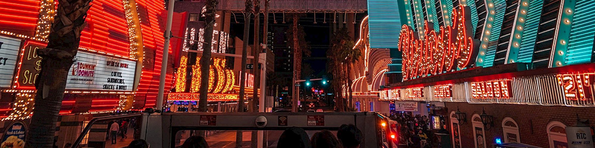 The image shows a vibrant, neon-lit street scene at night, featuring casinos and palm trees, likely depicting Fremont Street in Las Vegas.