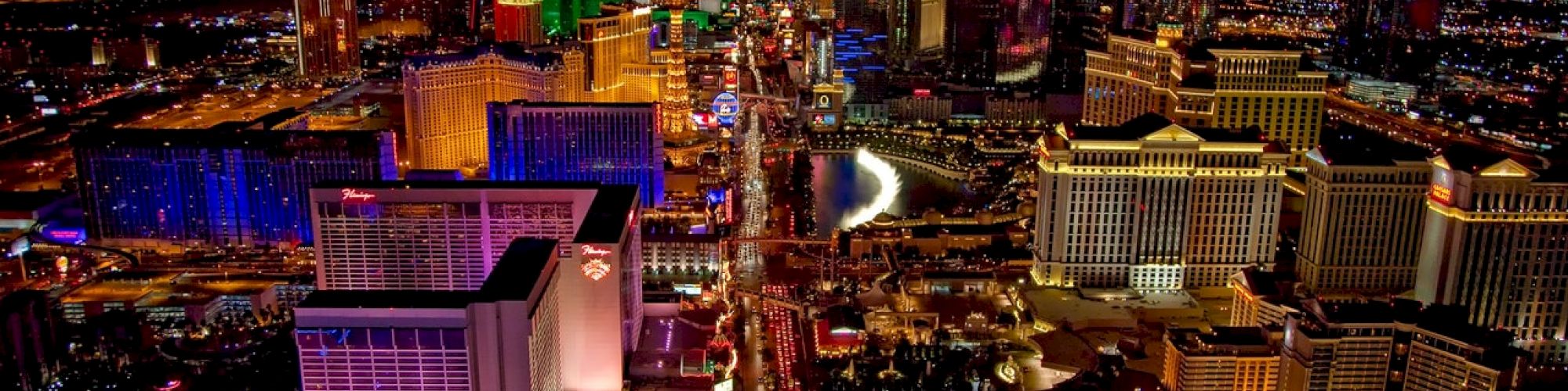 The image depicts an aerial view of the Las Vegas Strip at night, showcasing brightly lit hotels, casinos, and various buildings along a busy street.