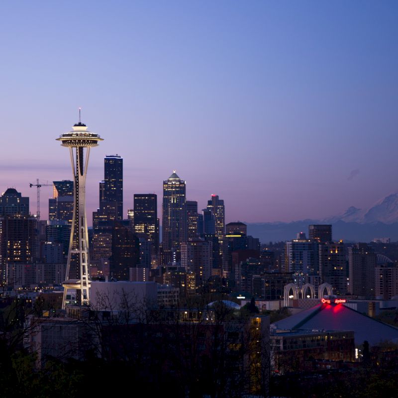 It's an evening or dusk view of a city skyline, featuring the Space Needle with Mount Rainier visible in the background.