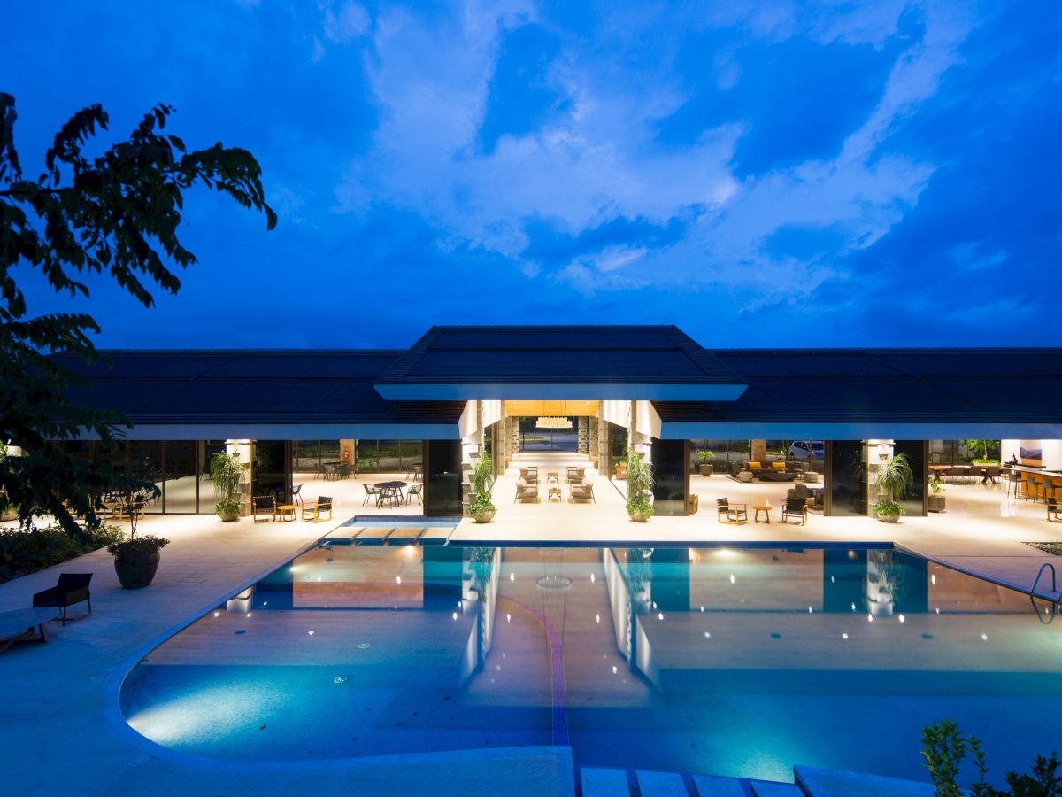 A luxurious outdoor pool area is illuminated at dusk, with modern architecture and seating areas visible in the background.