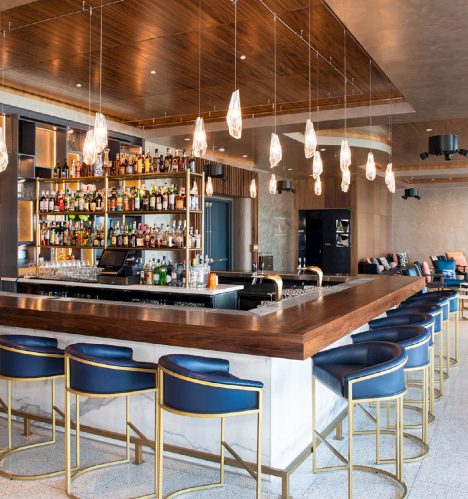 A modern bar with wooden accents, stylish seating, overhead lights, and a fully stocked bar in the center.