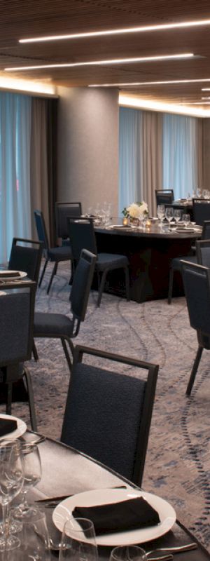 A modern event space with round tables set elegantly for dining, featuring black chairs, neatly arranged table settings, and soft lighting.
