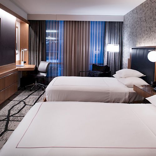 A hotel room with two neatly made beds, a large TV, a desk with a chair, and modern decor including lamps and patterned wallpaper ends the sentence.
