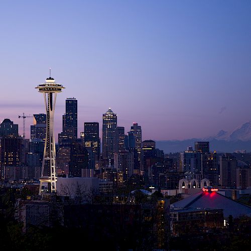 This image shows the Seattle skyline at dusk, featuring the Space Needle prominently, with Mount Rainier visible in the background.